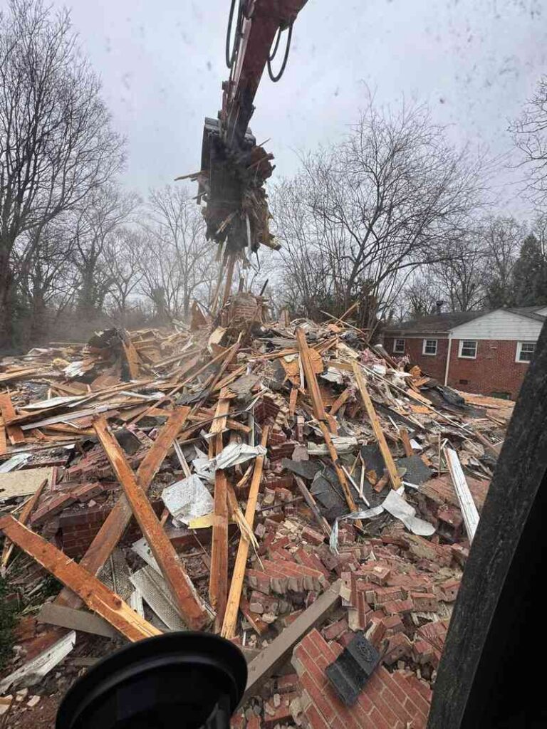 Excavator lifting demolition debris from a collapsed residential structure