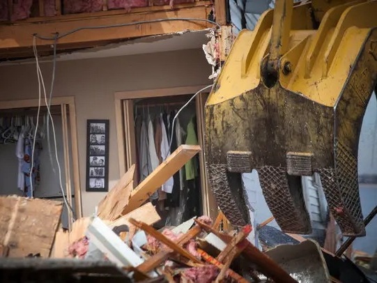 Excavator bucket removing debris from a storm-damaged house during interior demolition