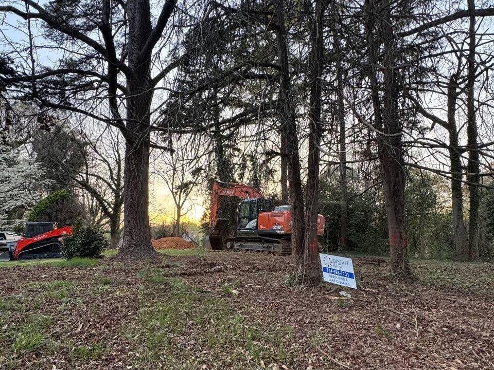 Excavator and skid steer clearing trees and brush on a wooded residential lot in the Charlotte area