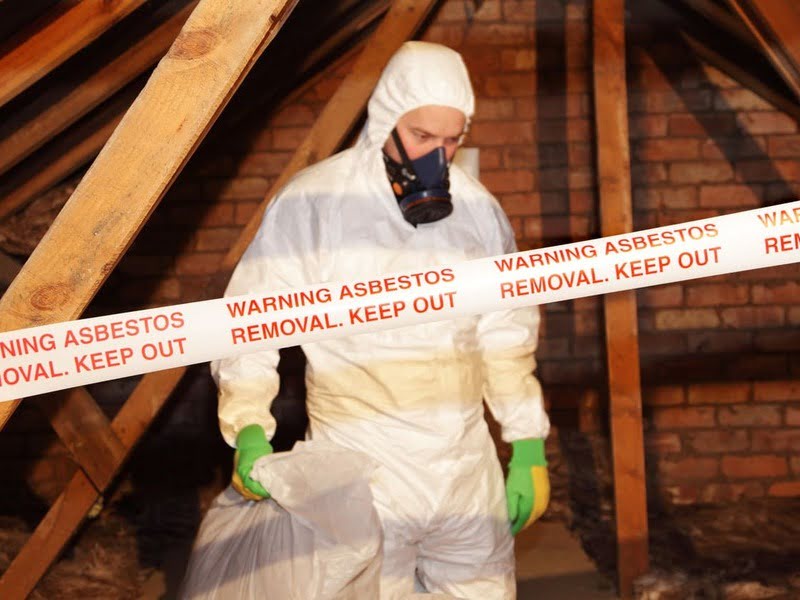 Asbestos abatement worker in protective gear during removal before demolition