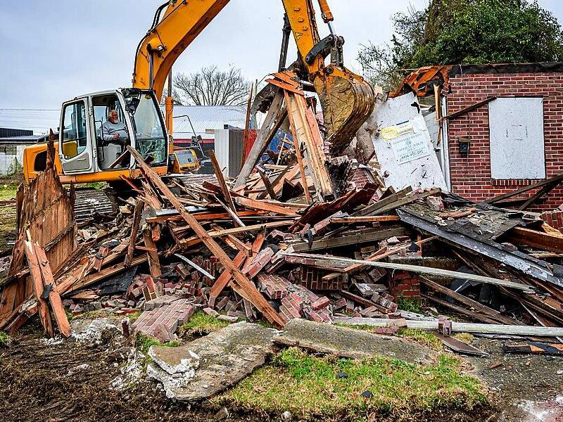 Excavator sorting wood, brick, and debris during a house demolition project