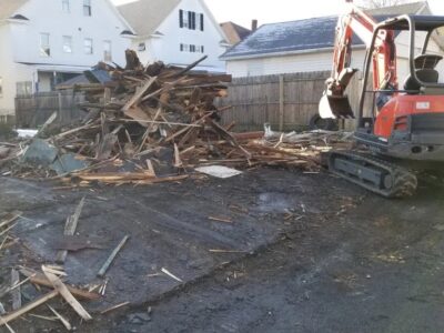 Mini excavator clearing wood debris after a detached garage demolition project