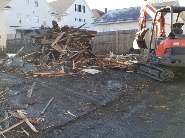 Mini excavator clearing wood debris after a detached garage demolition project